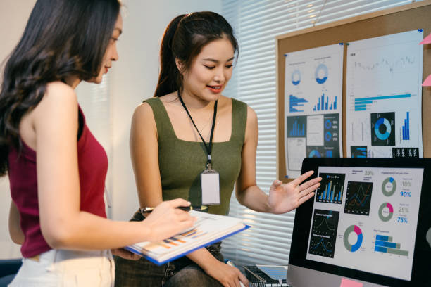 istock Two young asian businesswomen are discussing charts and graphs displayed on a computer screen and printed documents, analyzing data and collaborating on a project in their modern office 2194064447