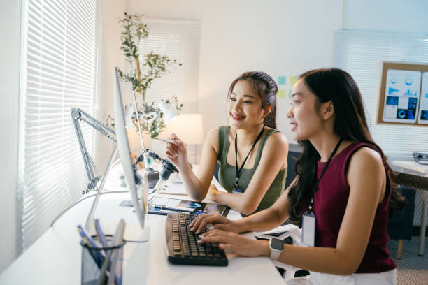 istock Two young asian businesswomen are working together on a desktop computer, discussing a project and analyzing data in a bright, modern office 2194064539