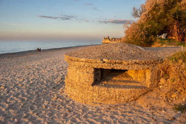Sandy beach of the Tyrrhenian sea. Bunker from the World War 2 illuminated by the light of sunset. Greenery in the background. Blue sky with small clouds. Campofelice di Roccella, Sicily, Italy.
