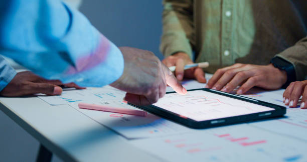 istock Close-up group of business working late, analyzing financial reports and charts on digital tablet surrounded by documents and graphs during strategic meeting at office night. Finance meeting. 2194068231