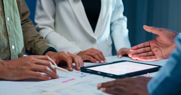 istock Close-up group of business working late, analyzing financial reports and charts on digital tablet surrounded by documents and graphs during strategic meeting at office night. Finance meeting. 2194068253