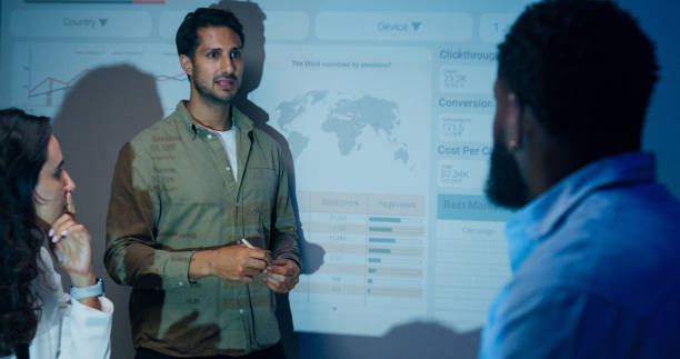 istock Group of businesspeople working late analyzing financial data displayed on projection screen while discussing strategy and planning for future business growth at office night. Finance meeting. 2194068278