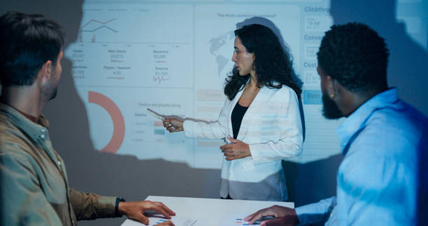 istock Group of businesspeople working late analyzing financial data displayed on projection screen while discussing strategy and planning for future business growth at office night. Finance meeting. 2194068286