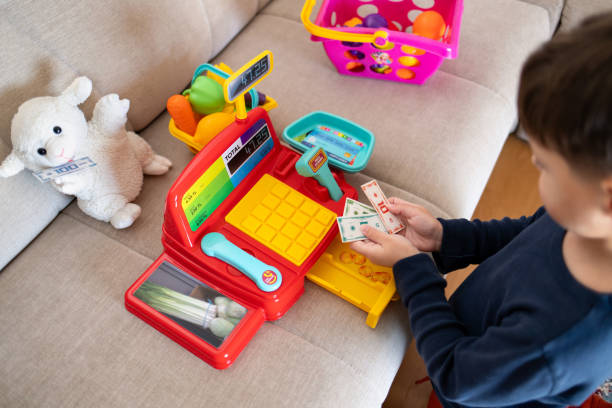 istock A boy is playing store at home with a toy cash register. 2194071256