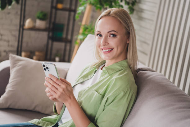 istock Charming young woman relaxing on a comfortable sofa while browsing her smartphone in a cozy, daylight-filled living room 2194074200