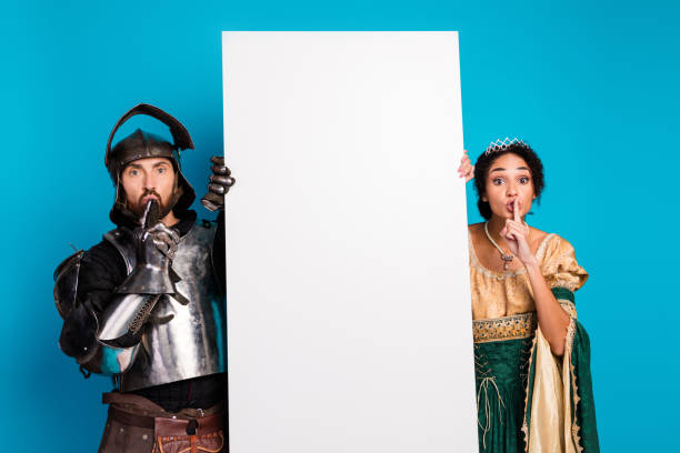 istock Couple in Royal and Knight Costumes Holding Banner Against Solid Blue Background 2194074820