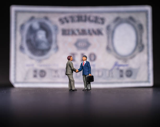 istock Two men shaking hands in front of a large bank note.. 2194074837
