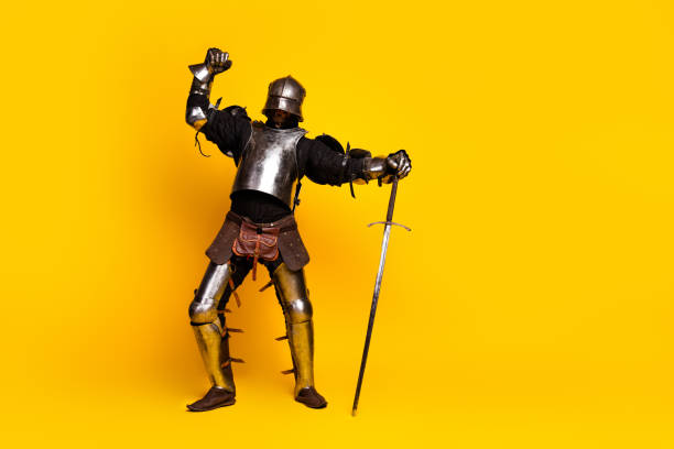 istock Young man dressed in medieval knight's armor striking a heroic pose against a vibrant yellow background 2194075752