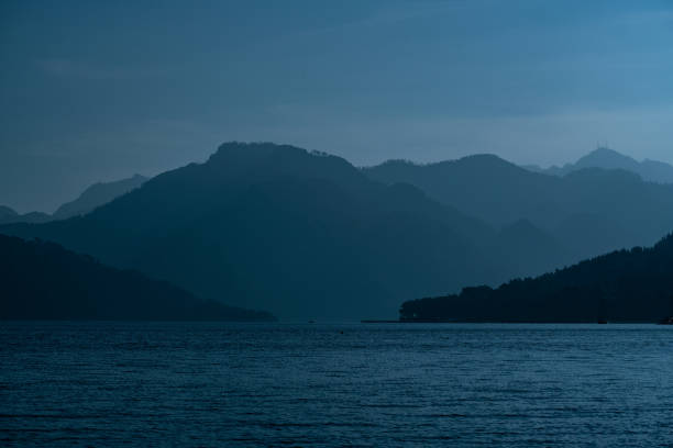 A tranquil image of distant mountains and water under a twilight ambiance, creating a calm and serene mood. The silhouette of the landscapes blends harmoniously into the night.