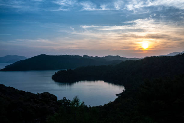 Scenic view of a peaceful lake surrounded by forested mountains during a captivating sunset, creating a tranquil atmosphere perfect for relaxation and nature appreciation, showcasing harmony between land and water.