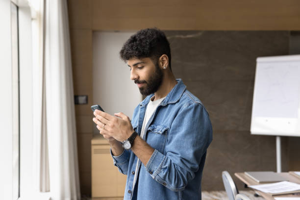 istock Young male office employee using smartphone standing in modern workspace 2194082981