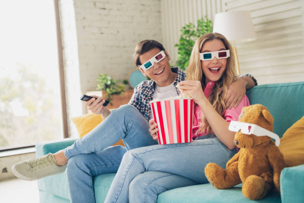 istock Young couple enjoying popcorn and wearing 3D glasses while relaxing at home 2194085137