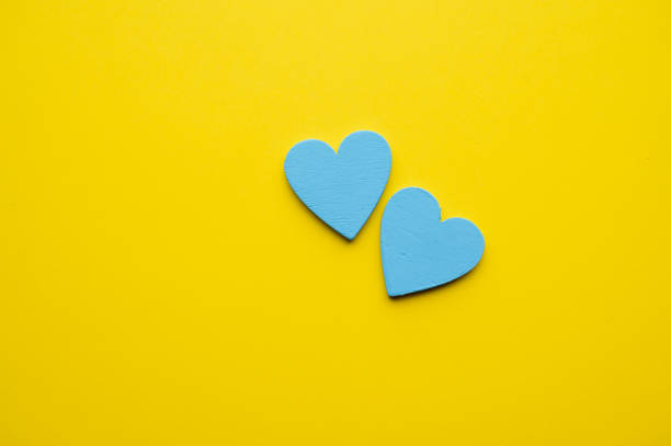 Two blue heart shapes placed together on a bright yellow background. The vivid color combination symbolizes love, harmony, and joy in a minimalist design.
