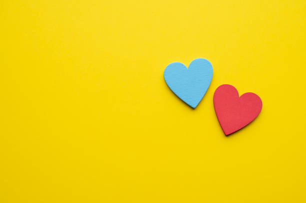 A blue heart and a red heart arranged together on a vibrant yellow background. The bright and contrasting colors evoke feelings of love, positivity, and energy in a simple composition.