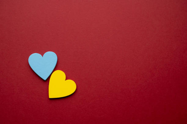 A blue heart paired with a yellow heart placed against a deep red background. The striking color combination symbolizes harmony, positivity, and love in a bold yet balanced composition.