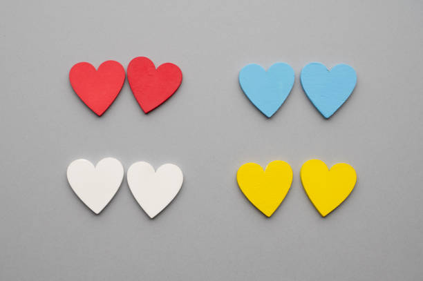 Four pairs of colorful heart shapes arranged neatly on a gray background. Each pair consists of hearts in red, blue, white, and yellow, symbolizing love and diversity.