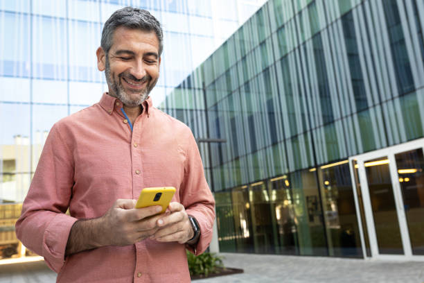 istock Smiling businessman using smartphone outside office building 2194098753