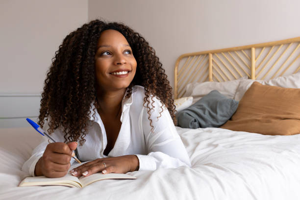 istock Young woman lying on bed writing in notebook and smiling 2194098784