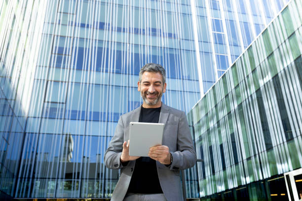 istock Smiling businessman using digital tablet in front of modern office building 2194098915