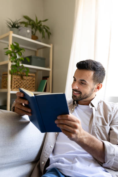 istock Young man relaxing on sofa reading a book at home 2194098938