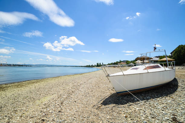 A tranquil scene of a white boat resting on a pebble beach, with calm waters and a clear blue sky serving as the backdrop, depicting serenity and coastal leisure