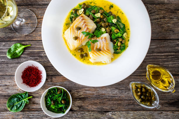 istock Fish dish - fried cod with spinach and capers in saffron sauce on wooden table 2194103656
