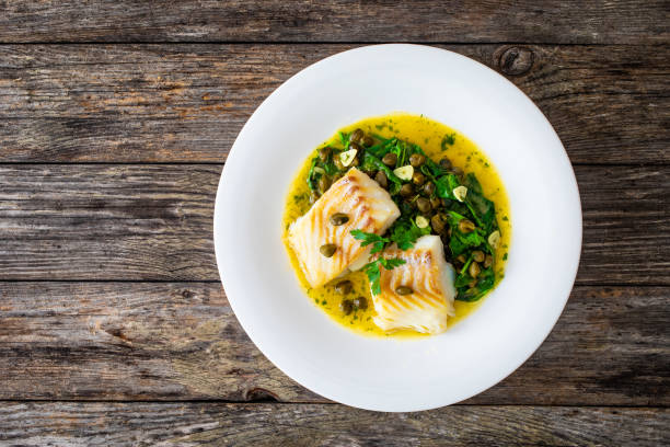 istock Fish dish - fried cod with spinach and capers in saffron sauce on wooden table 2194103685