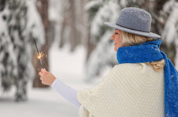 Smiling woman holding sparklers and enjoying on a snowy mountain during Christmas holidays