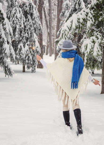 Smiling woman holding sparklers and enjoying on a snowy mountain during Christmas holidays