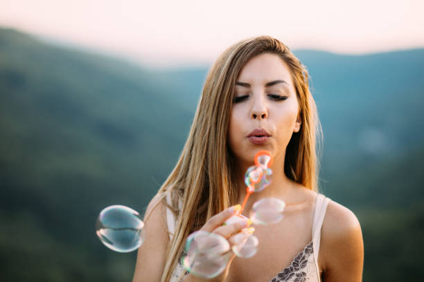 istock Beautiful Young Woman Blowing Soap Bubbles Outdoors on a Summer Day 2194105603