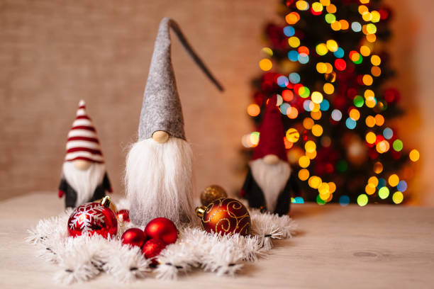 Decorative holiday gnomes surrounded by festive ornaments and white garland, placed in front of a beautiful bokeh Christmas tree, creating a charming and cozy seasonal atmosphere.