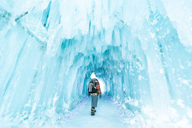 A frozen cave with a woman walking in it enjoying the views.