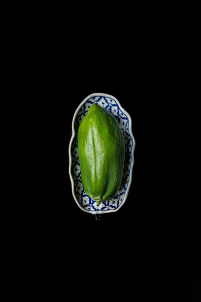 The image captures a vibrant green starfruit, also known as carambola, placed on a beautifully designed traditional patterned plate. The deep black background enhances the fruit's natural color and shape, highlighting its unique ridges and glossy surface. This minimalist composition is perfect for emphasizing the exotic appeal of this tropical fruit.