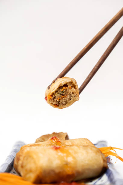 Crispy Thai spring rolls filled with chicken and vegetables, Held by wooden chopsticks, Against a clean white background, Highlighting authentic Thai street food culture
