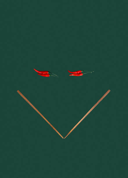 This minimalist image showcases two vibrant red chili peppers paired with wooden chopsticks, arranged in a striking geometric design on a dark green backdrop. The simplicity and contrast in the composition highlight the bold colors and textures, symbolizing the essence of Asian cuisine and contemporary design. Perfect for use in culinary, dining, or food art projects.