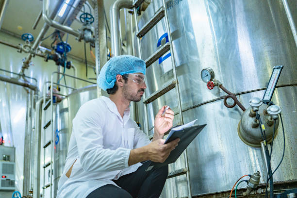 istock Worker examining an industrial tank and recording data on a clipboard, emphasizing the importance of safety, quality assurance, and technological advancement in industrial environments. 2194114617