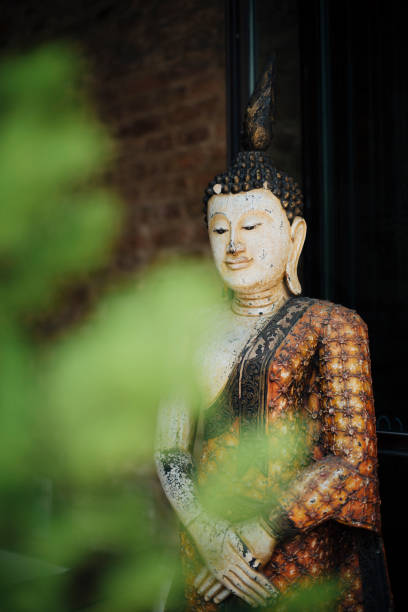 istock A serene Buddha statue in traditional attire, Partially framed by soft greenery, With a brick wall background, Symbolizing peace, spirituality and cultural heritage 2194114679