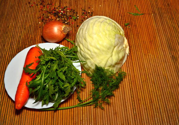 fresh vegetables of different types on a dark background for salad grass rakula tomatoes peppers wooden spoon onion cabbage carrots and other vegetables tomato, sweet pepper, greens, cucumber, light wooden spoon, onion, arugula herb with meat taste