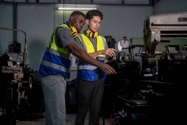 istock Two industrial engineers in high-visibility vests collaborate in a workshop. One holds tablet, pointing at equipment, discussing plans. Ear protection and gloves emphasize safety and professionalism. 2194121576