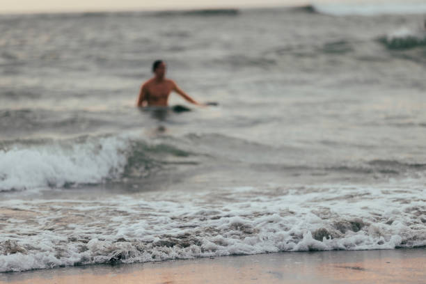 Youn man is walking on Canggu beach after surfing ocean.Canggu beach - Bali Island.