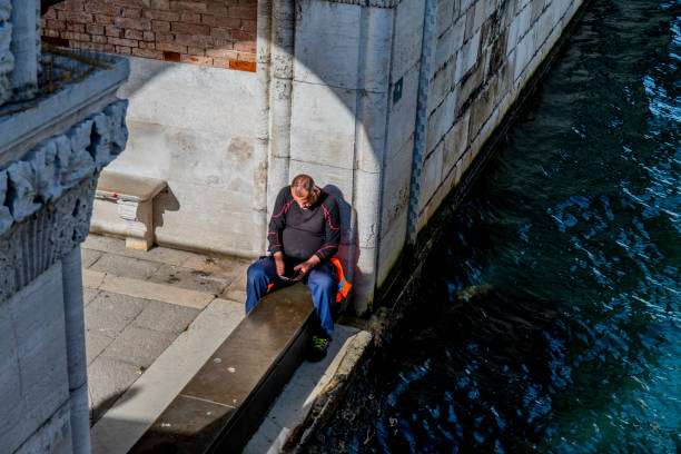 Venice, Italy_Nov 4, 2024.\nMan uses his mobile phone beside a canal in Venice.