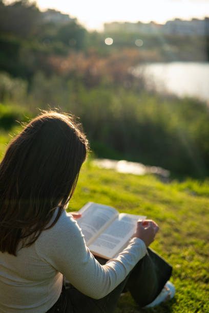 istock Young woman relaxing on the grass while reading a book in an urban park. 2194155667