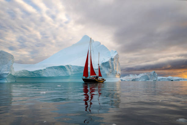 istock red sailboat sailing among floating icebergs in Disko Bay glacier with orange sunset during polar summer midnight solar season. Ilulissat, Greenland 2194166457