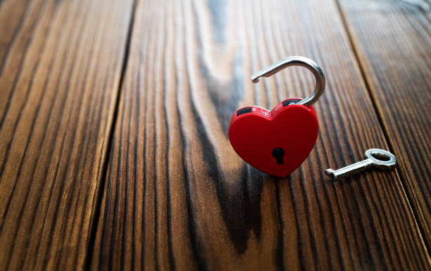 istock Red heart shaped padlock with silver key on wooden table 2194166525