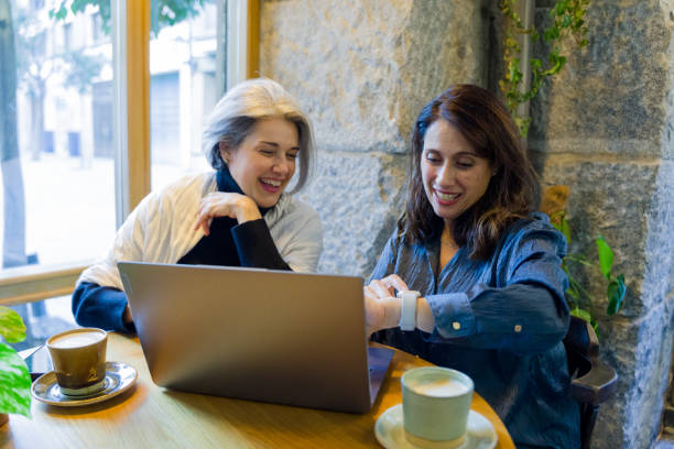 istock Two mature women laughing and using a laptop in a cafe 2194173999
