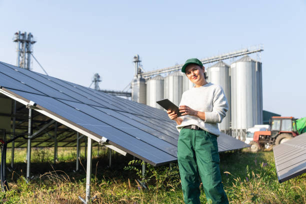 istock Female farmer with digital tablet on a modern farm using solar panels. Agricultural silos in the background 2194174039