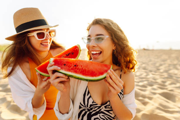 istock Smiling two women eating watermelon on beach. 2194176822