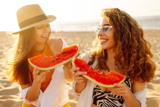 istock Smiling two women eating watermelon on beach. 2194176831