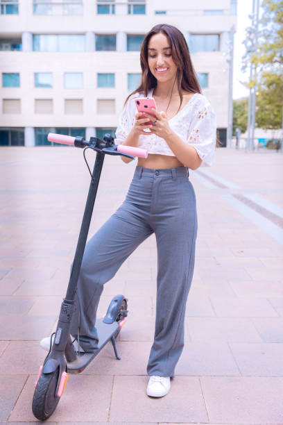 istock Happy Young Woman Using Smartphone Next to Electric Scooter Outdoors.Vertical 2194177387