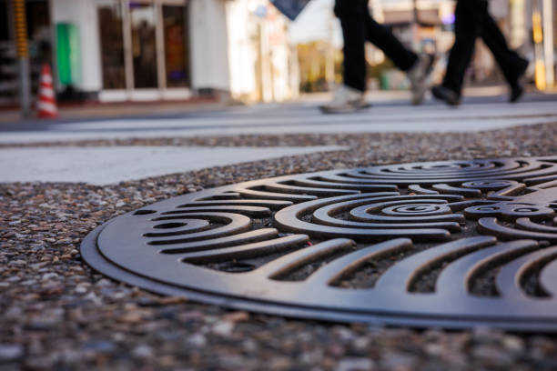 A weathered and rusty circular cast iron manhole cover with a textured pattern, set against dark asphalt, urban element